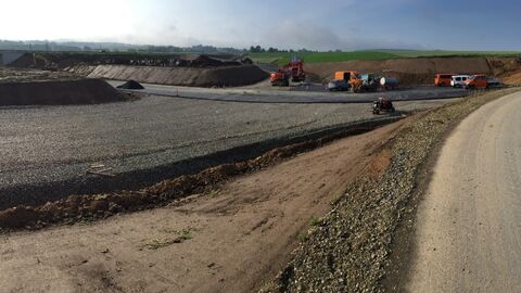 Unfertige Straße mit Baumaschinen im Hintergrund fotografiert im Sonnenschein - Bereich der neuen Anschlusstelle B83 / K47(neu) – Baustellenumfahrung für die Errichtung von BW 6