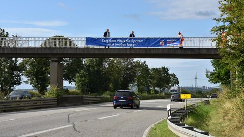 Corona-Pandemie - Hessen Mobil unterstützt im Oktober den Aufruf der Hessischen Landesregierung zum Testen und Impfen mit dem Anbringen von Bannern und dem Aufstellen von LED-Tafeln an zahlreichen Bundesstraßen.  Personen bringen ein Banner an dem Geländer einer Brücke an.
