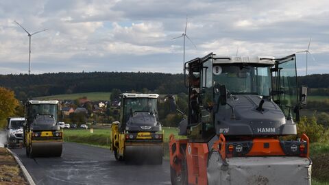 Pilotprojekt in Osthessen: Die Erneuerung der L 3169 zwischen Hechelmannskirchen und Kreisgrenze erfolgt zum Teil unter Einbau von Niedrigtemperatur-Asphalt. Vor allem Arbeitsschutz- und Umweltschutzgründe spielten bei dieser Entscheidung eine Rolle.  Baufahrzeuge fahren auf einer neuen Straße.
