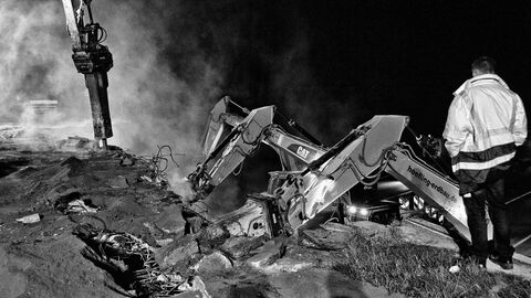 Ein Mann mit Arbeiter-Jacke mit Reflektoren beobachtet die Abbrucharbeiten