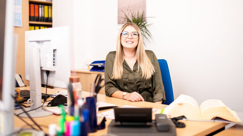 Eine Mitarbeitern von Hessen Mobil sitzt an Ihrem Arbeitsplatz und lächelt in die Kamera.