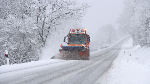 Tiefverschneite Straße mit Räumfahrzeug