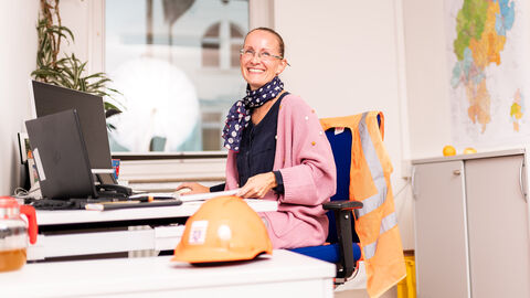 Freundlich lächelnde Hessen Mobil-Mitarbeiterin sitzt vor ihrem Computer am Schreibtisch