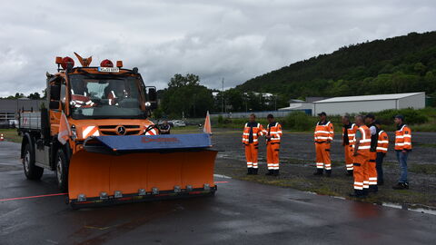 Trainingstag Schneepflugmeisterschaft 17 Ein Unimog steht in der Parkposition. Mehrerer Teammitglide stehen daneben