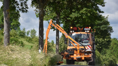 Mäharbeiten SM Wolfshagen 4 Orangefarbener Unimog von hessen Mobil mäht mit einem vormontierten Balkenmäher hohes Gras am Straßenrand