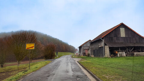 Schadhafte Landesstraße mit Haus am rechten Rand 