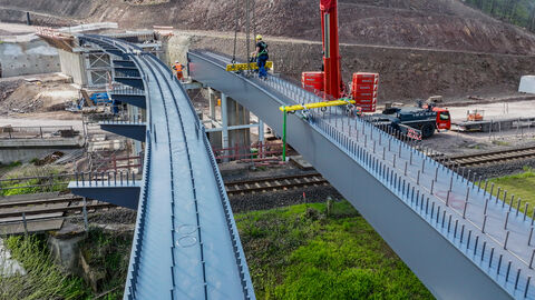 Ein Drohnenbild zeigt den Einbau von sehr langen Brückenfertigteilen aus Stahl an einer Brücke.