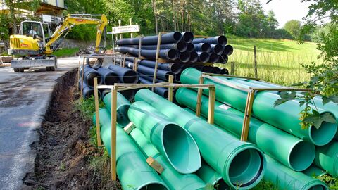 Grüne und schwerze Kunsstoffrohre liegen aufgestapelt am Straßenrand