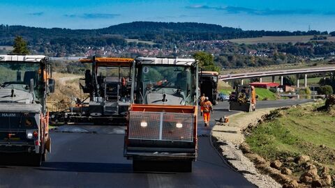 Mehrere Baumaschienen stellen eine Fahrbahndecke her.