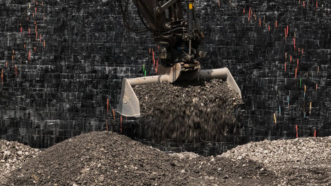 Ein Bagger füllt mit seiner Baggerschaufel Schotter in die Waben