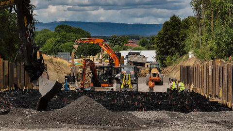 Ein Bagger füllt mit seiner Baggerschaufel Schotter in die Waben