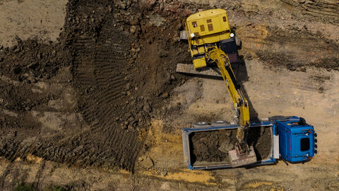Drohnenaufnahme eines Baggers der Erdaushub auf einen LKW lädt