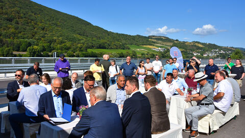 Das Publikum der Verkehrsfreigabe sitzt bei herrlichem Sonnenschein an Festbankgarnituren