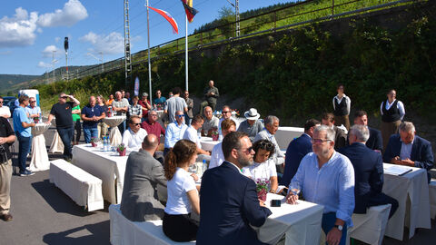 Das Publikum der Verkehrsfreigabe sitzt bei herrlichem Sonnenschein an Festbankgarnituren
