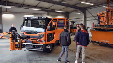 Azubitag 2023 auf der SM Alten-Buseck -8 Die Azubis stehen um ein orangenes Multicar in einer der Fahrzeughallen