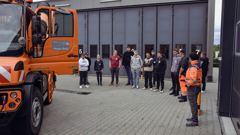 Azubitag 2023 auf der SM Alten-Buseck -10 Die Azubis stehen um ein orangenes Räumfahrzeug auf dem Hof