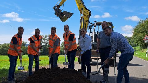 einieg Männer mit Spaten vor einem Erdhaufen - im Hintergrund ein Bagger