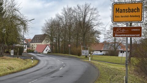Ortschild von Mansbach im Vordergrund - der Beginn der Ortsdurchfahrt im Hintergrund