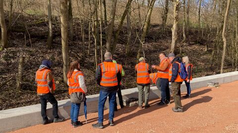 Eine Gruppe in orangenen Warnwesten schaut sich die Stützmauer genauer an