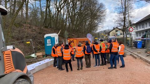 Eine Gruppe in orangenen Warnwesten läuft über die Baustelle